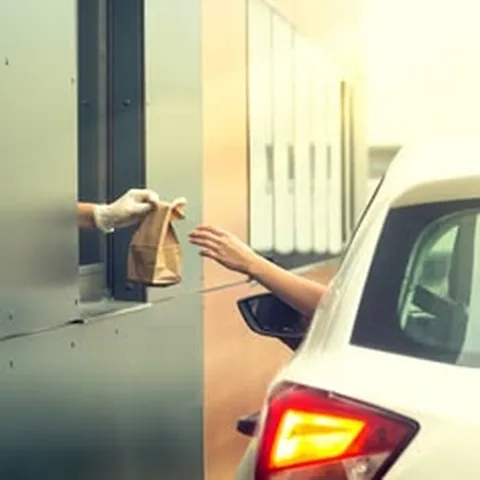 Driver reaching out of a car window to take a paper bag at a fast food drive-thru