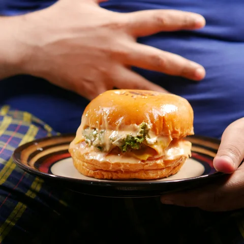 Man holding a burger with a hand resting on his stomach